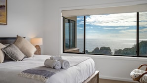 A bedroom with a large window, a bed with pillows, a rolled towel, and a lamp. - Noah's 46 Cliff Road (Forster)