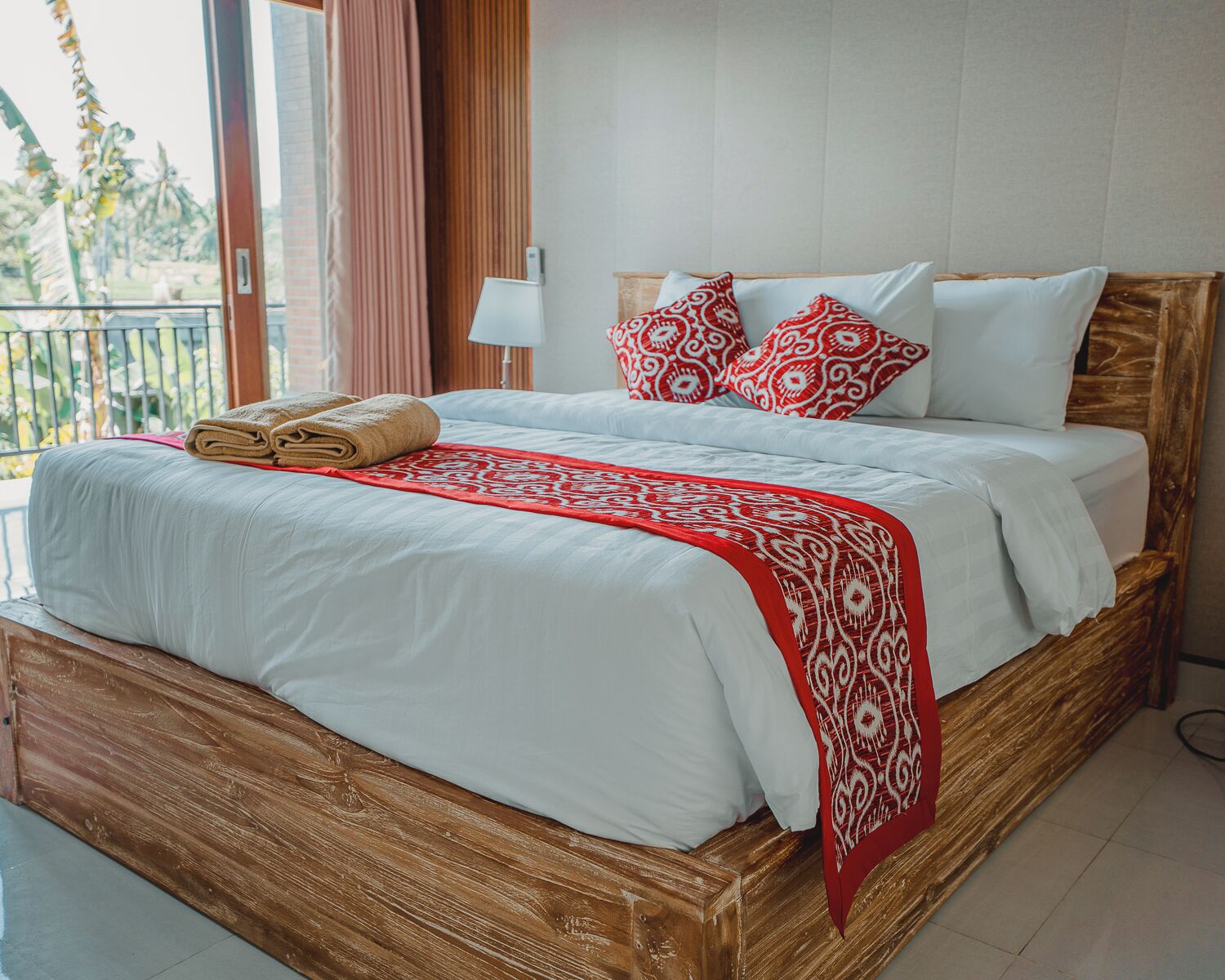 A neatly made bed with white linens, a red patterned throw, and multiple pillows.