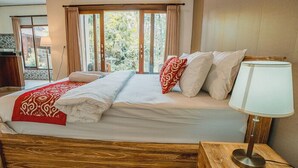 A bedroom with a wooden bed, a bedside lamp, and a window with curtains. - Rizky Guesthouse (Ubud)