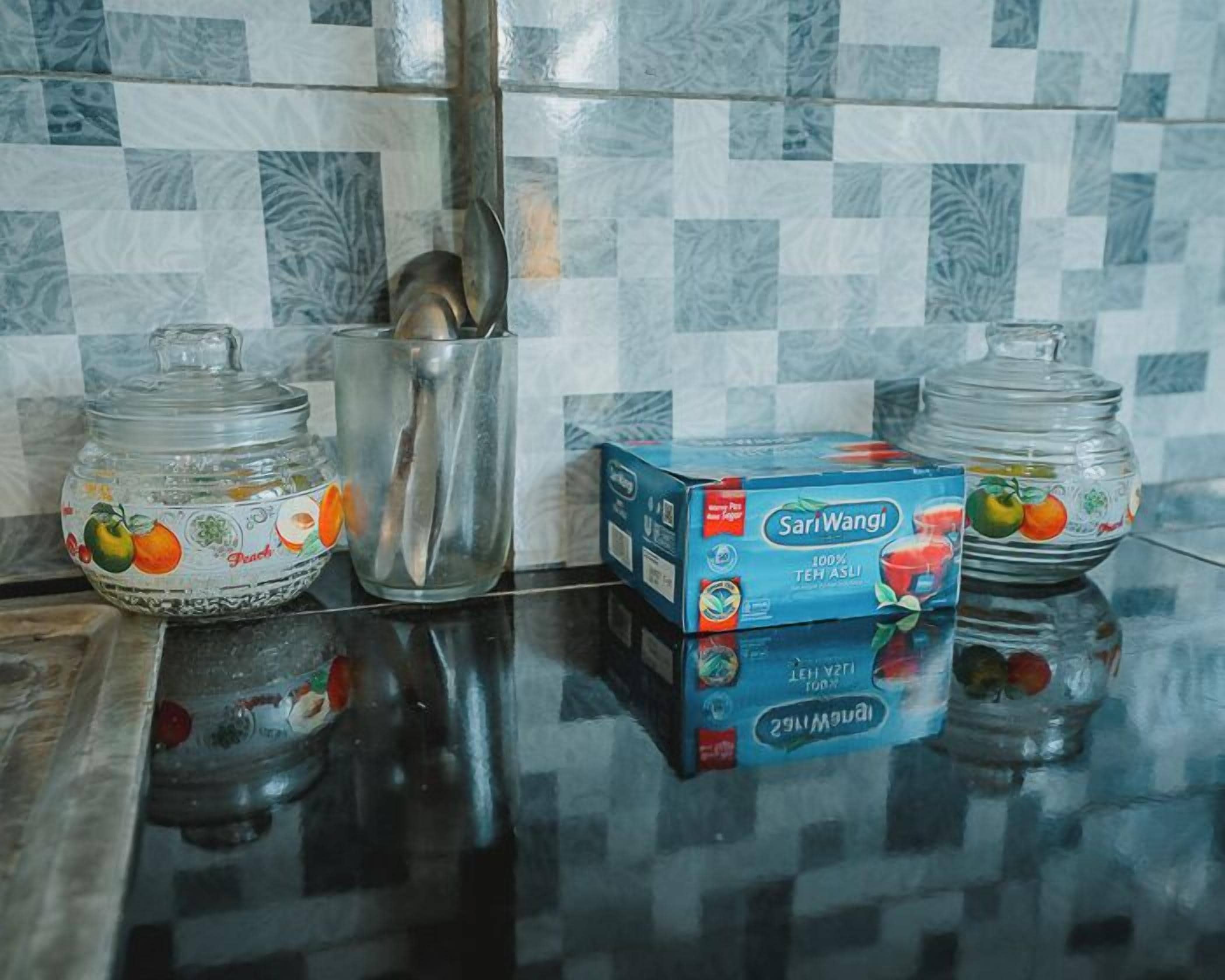A kitchen counter with two glass jars, one with a fruit design, a metal container, and a box of Sari Wangi tea.