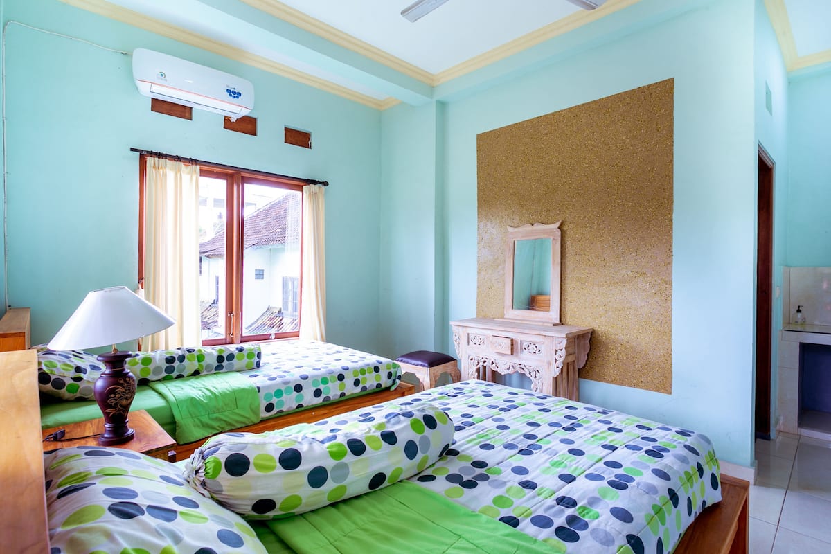 A room with two beds, a wooden dresser, a mirror, and an air conditioning unit.