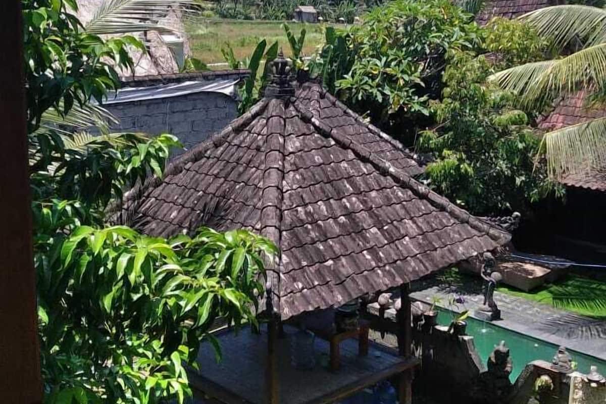 A traditional thatched-roof pavilion surrounded by lush greenery and a clear blue sky.