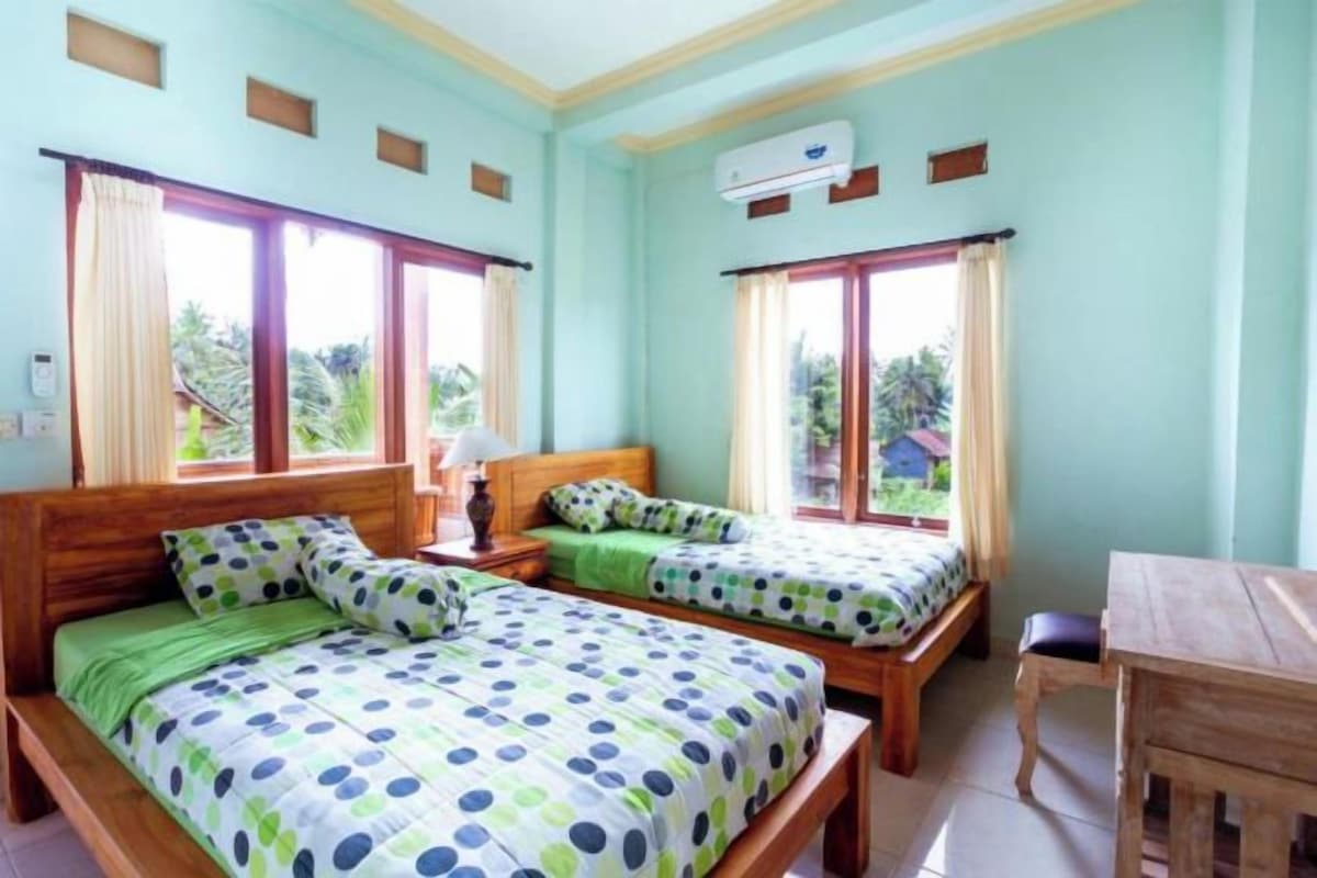 A room with two beds, a wooden table, and large windows.