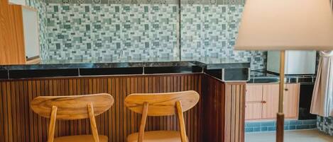 A kitchen with a tiled backsplash, wooden bar counter, and two wooden bar stools.