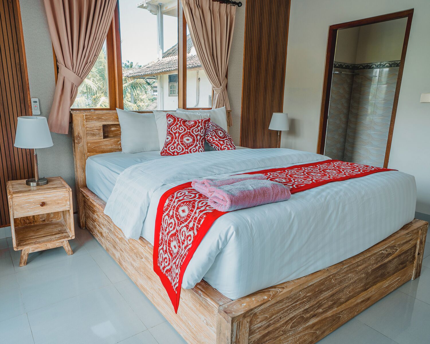 Una cama de madera con ropa de cama blanca y roja, dos mesitas de noche y vistas al exterior.