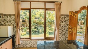 A kitchen with a large window, a refrigerator, and a wooden cabinet. - Rizky Guesthouse (Ubud)