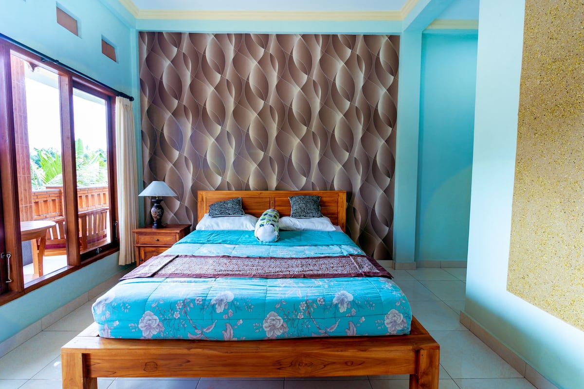 A bedroom with a bed, wooden headboard, and a view of the outdoors through a sliding door.