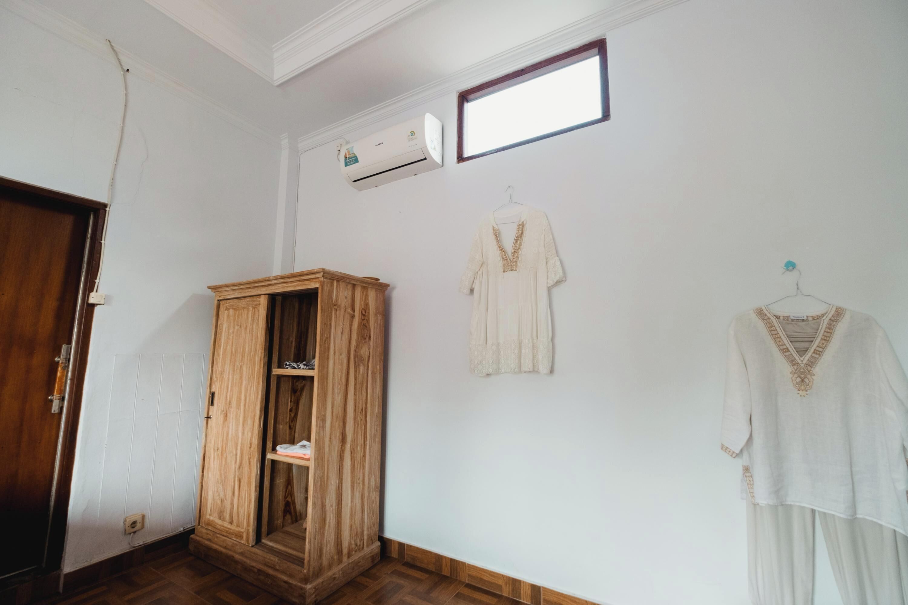 A room with a wooden wardrobe, a hanging light fixture, and a wall-mounted air conditioner.