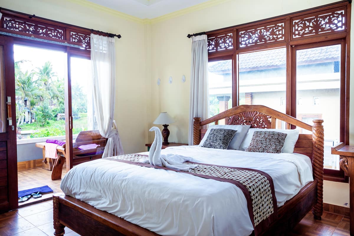 A spacious bedroom with a large bed, a wooden headboard, and a view of a garden through a sliding door.