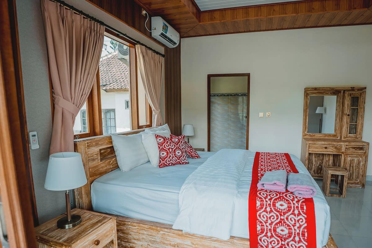 A bedroom with a bed, bedside tables, a mirror, and an air conditioning unit.