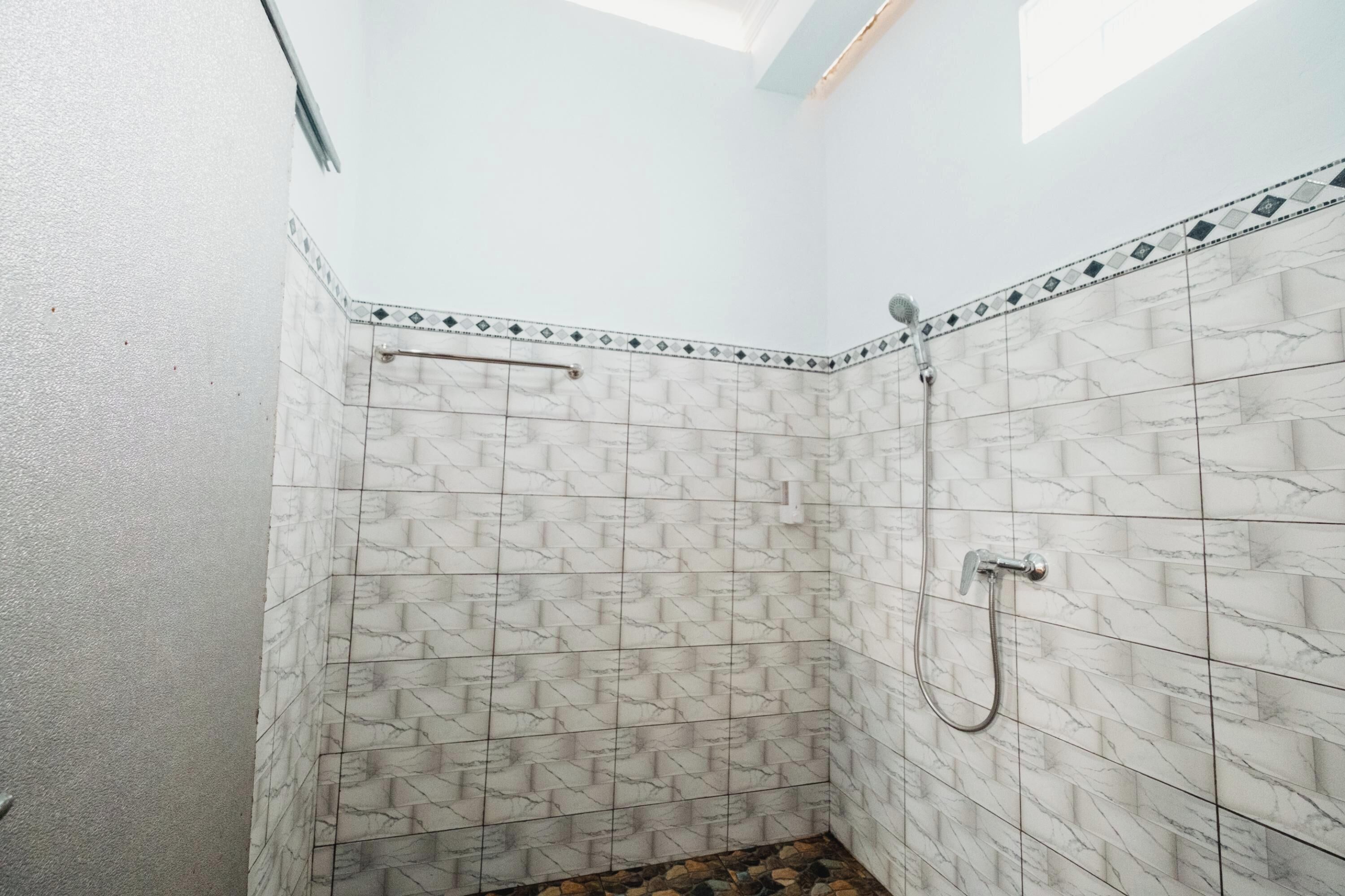 A shower with white marble tiles and a handrail.