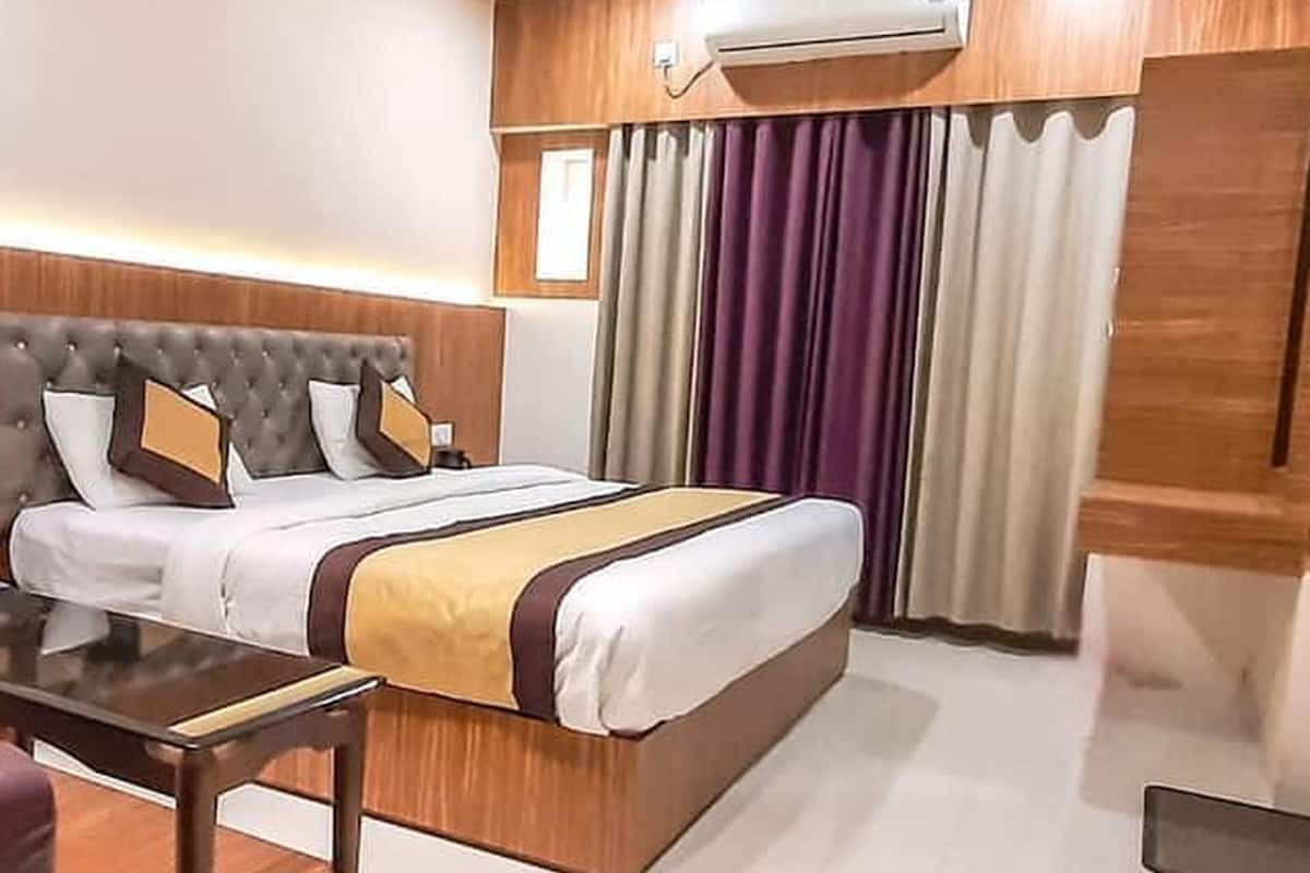 A modern hotel room with a large bed, wooden headboard, and a built-in air conditioning unit.