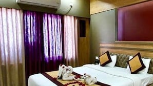 Una habitación de hotel con cama, mesita de noche, unidad de aire acondicionado, cortinas y cabecero.