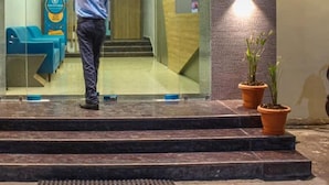 Un hombre camina hacia una zona de recepción con puerta de vidrio, una zona de estar azul y una planta en maceta en los escalones.