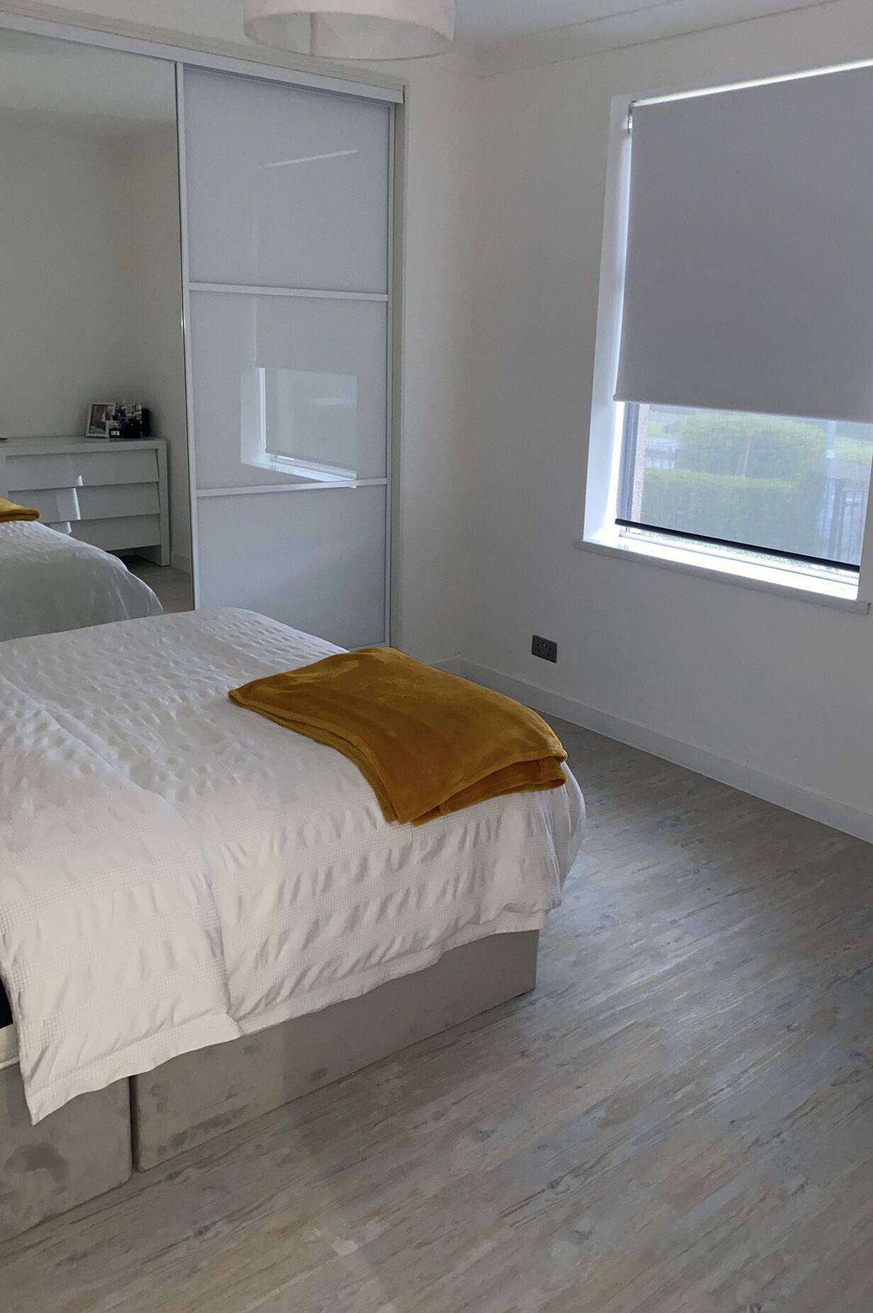 A bedroom with a bed, a wardrobe, a desk, and a window with a blind.