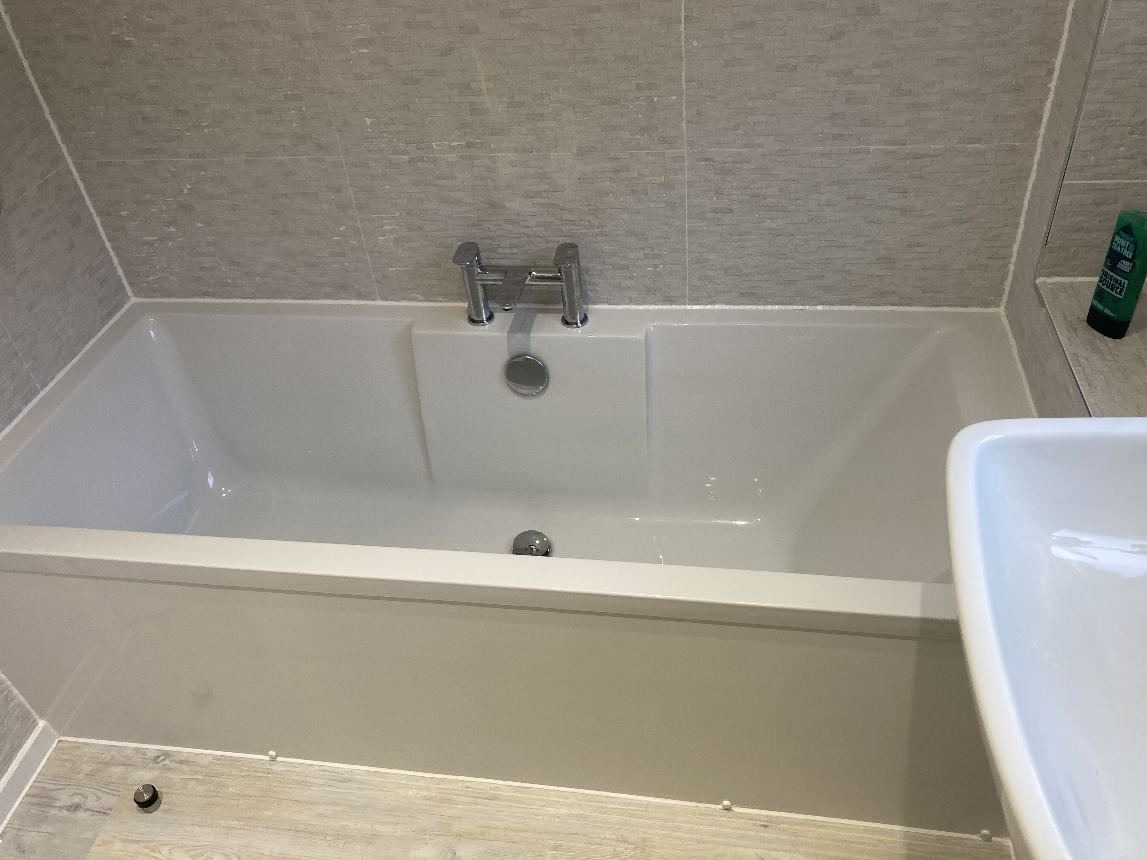 A bathtub with a faucet and a drain, a wooden floor, and a tiled wall.