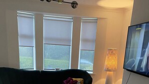 A living room with a sectional sofa, a round ottoman, and a floor lamp. - COP 26immaculate Newly Refurbished2 bed in Glasgow (Glasgow)