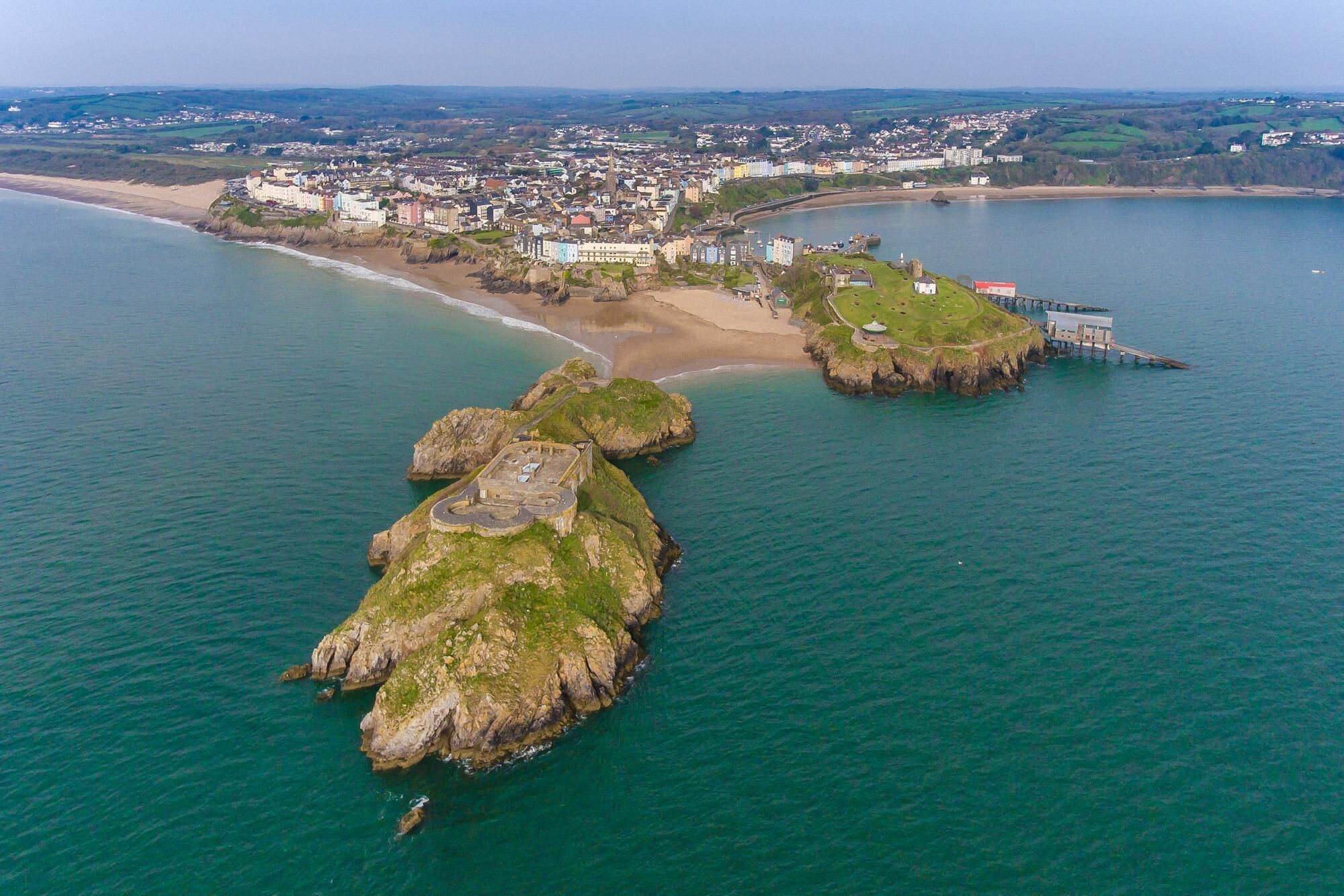 An aerial view of a coastal town with a prominent rocky outcrop and a sandy beach.