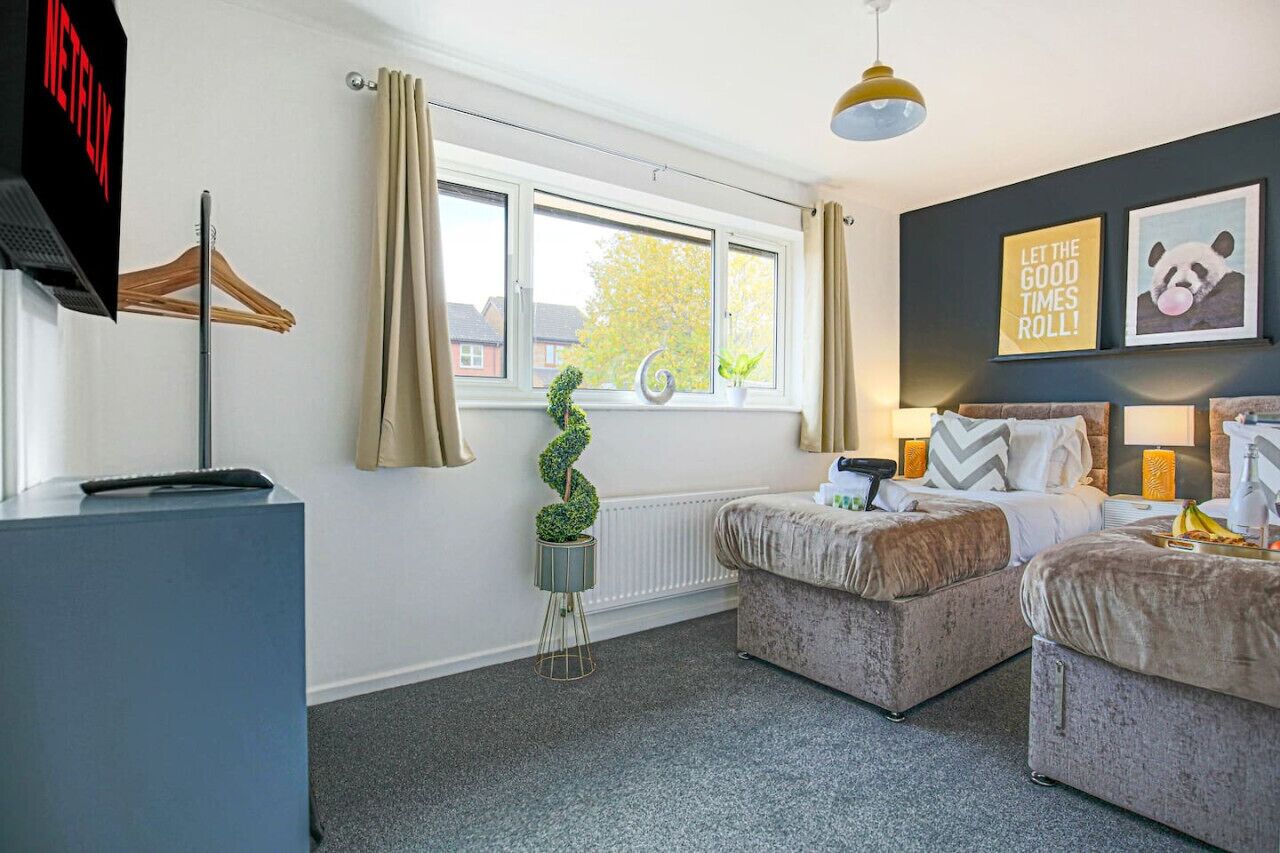 A modern bedroom with two beds, a desk, and a window with curtains.