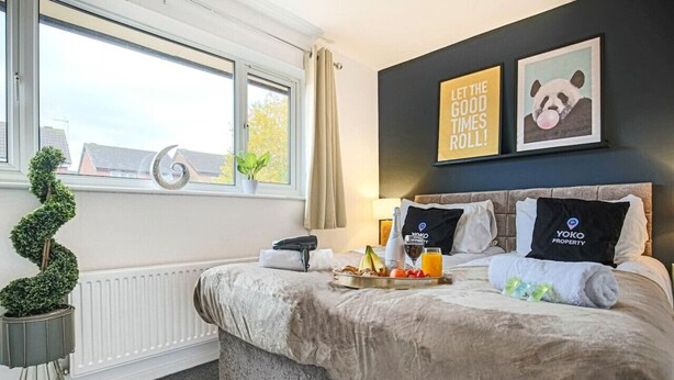 Ein Hotelzimmer mit Bett, Fenster mit Blick, einer Pflanze und einer Wand mit zwei gerahmten Bildern.