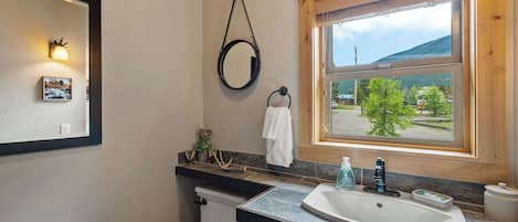 Un baño con inodoro, lavamanos, espejo y ventana con vistas a la vegetación.