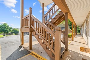 A wooden staircase leading to a covered porch area with a clear view of the street and greenery in the background.