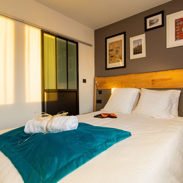 A hotel room with a bed, a window with blinds, and framed pictures on the wall. - Berti Hôtel Mulhouse Centre Gare (Mulhouse)