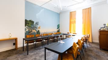 A conference room with a long table, chairs, a painting on the wall, and a view through the window.