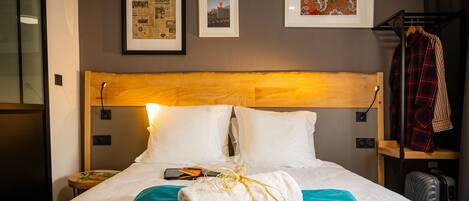 Una habitación de hotel con una cama bien hecha, un cabecero de madera y una pared con tres cuadros enmarcados.
