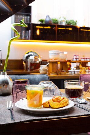 Ein Frühstückstisch mit einem Croissant, einem Glas Orangensaft und einem Glas dunklem Getränk.