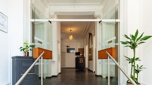 Entrada de hotel con mostrador de recepción, una escalera con bandas amarillas de seguridad y plantas en macetas.