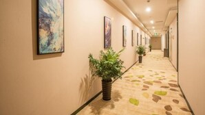 Um corredor de hotel com quadros nas paredes, plantas em vasos e um tapete estampado.