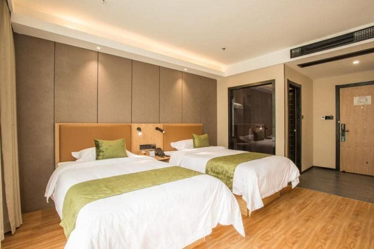 A hotel room with two beds, wooden flooring, and a large window.