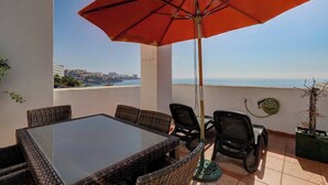 A terrace with a table and chairs, a red umbrella, and a view of the sea. - Sea Views Beachfront Apt, Large Private Terrace (Benalmádena)