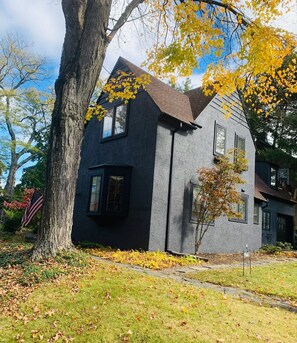 A modern two-story house with a dark gray exterior, a sloped roof, and a large tree in the foreground. - Historic Rustic Kingston Home. (KINGSTON)