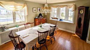 A dining room with a wooden table, six chairs, a chandelier, a clock, and a window with curtains. - Historic Rustic Kingston Home. (KINGSTON)