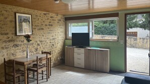Un coin repas avec une table et des chaises en bois, un téléviseur posé sur un meuble, et une fenêtre donnant sur un paysage verdoyant.