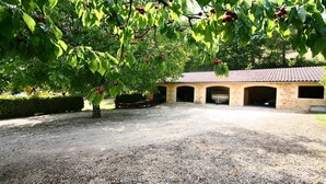 Une allée de gravier mène à un bâtiment doté d’un toit en tuiles et de plusieurs portes de garage ouvertes.