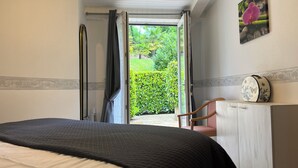 Une chambre à coucher comprenant un lit, une chaise, une armoire et donnant sur un jardin grâce à une porte ouverte.