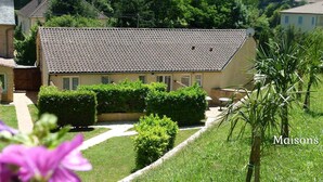 Une maison avec un toit en tuiles, un jardin bordé de haies et une antenne parabolique.