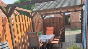 A patio with a table and chairs, a wooden fence, and a brick wall. - Vacation home, North Sea, Krummhörn, Upleward <br> (Krummhörn)