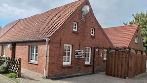 A brick house with a red-tiled roof, a wooden fence, and a paved driveway. - Vacation home, North Sea, Krummhörn, Upleward <br> (Krummhörn)