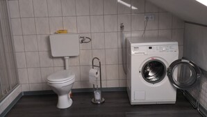 Une petite buanderie comprenant des toilettes, un lave-linge et un porte-serviettes.