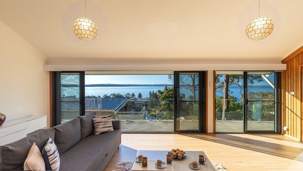 A modern living room with a large sliding glass door leading to a balcony with a view of the sea. - Sea La Vie 3 Warruga St, Corlette (Corlette)
