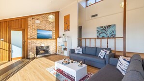 A living room with a fireplace, a sofa, a coffee table, and a TV mounted on a brick wall. - Sea La Vie 3 Warruga St, Corlette (Corlette)
