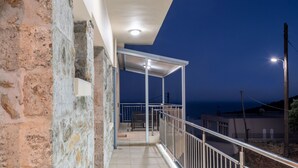 Ein Balkon mit Steinwänden, einem Metallgeländer und Blick auf das Meer im Dämmerlicht.