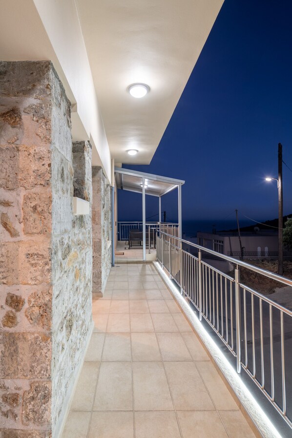 A balcony with stone walls, a metal railing, and a view of the sea at dusk.