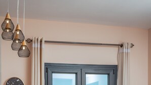 Ein Essbereich mit Tisch, roten Stühlen, einer schwarzen Tischdecke, einer Obstschale und Meerblick durch ein dunkel gefasstes Fenster.
