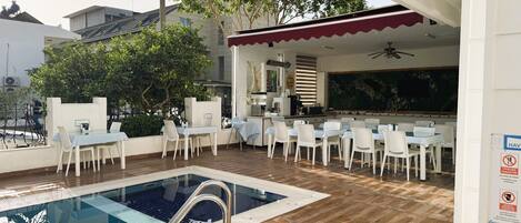 An outdoor pool area with a dining setup and a covered seating area.