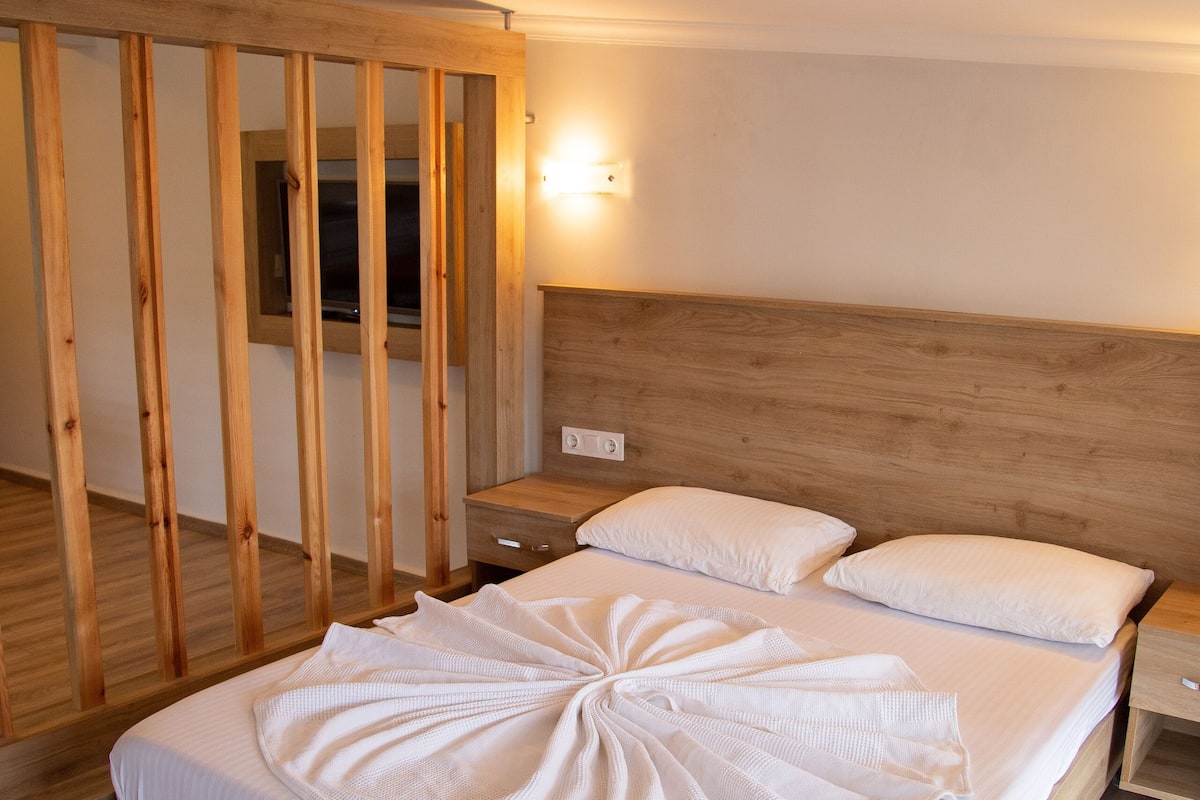 A neatly made bed with white linens, a wooden headboard, and a nightstand with a lamp.